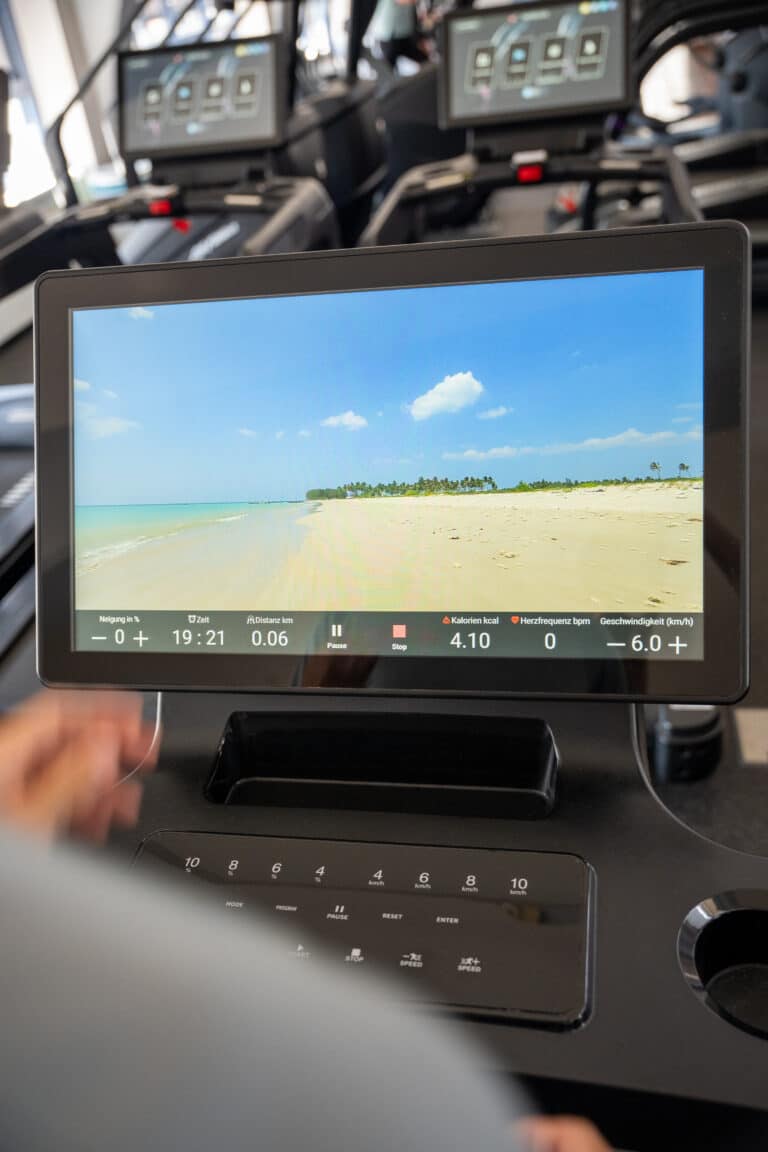 Laufband-Display im INJOYmed Dresden zeigt ein Strandvideo während des Ausdauertrainings